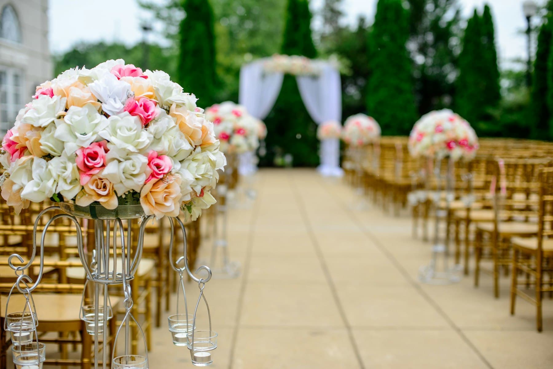 Outdoor ceremony aisle lined with flower arrangements and gold chairs